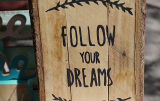 A sign carved into wood saying "follow your dreams"