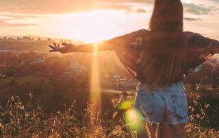 Woman stands on mountain over field under cloudy sky at sunrise